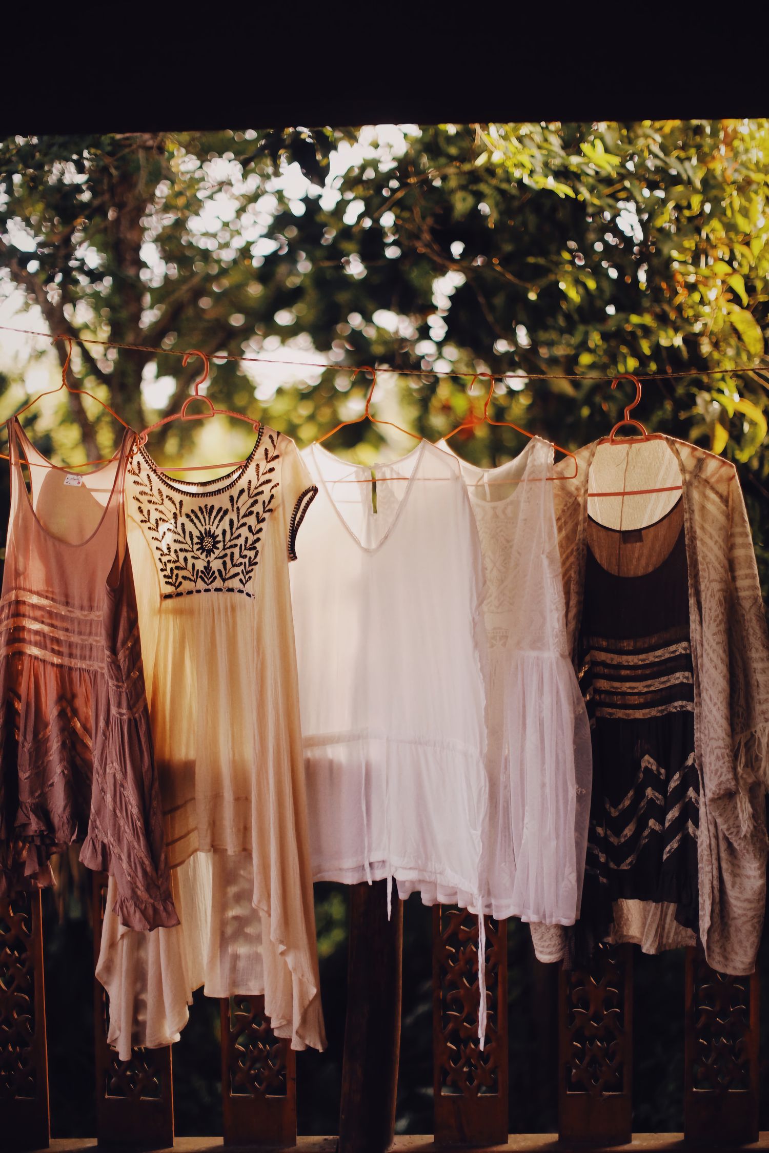 Vintage bohemian dresses on hangers outside in natural light, for a rustic fashion theme.