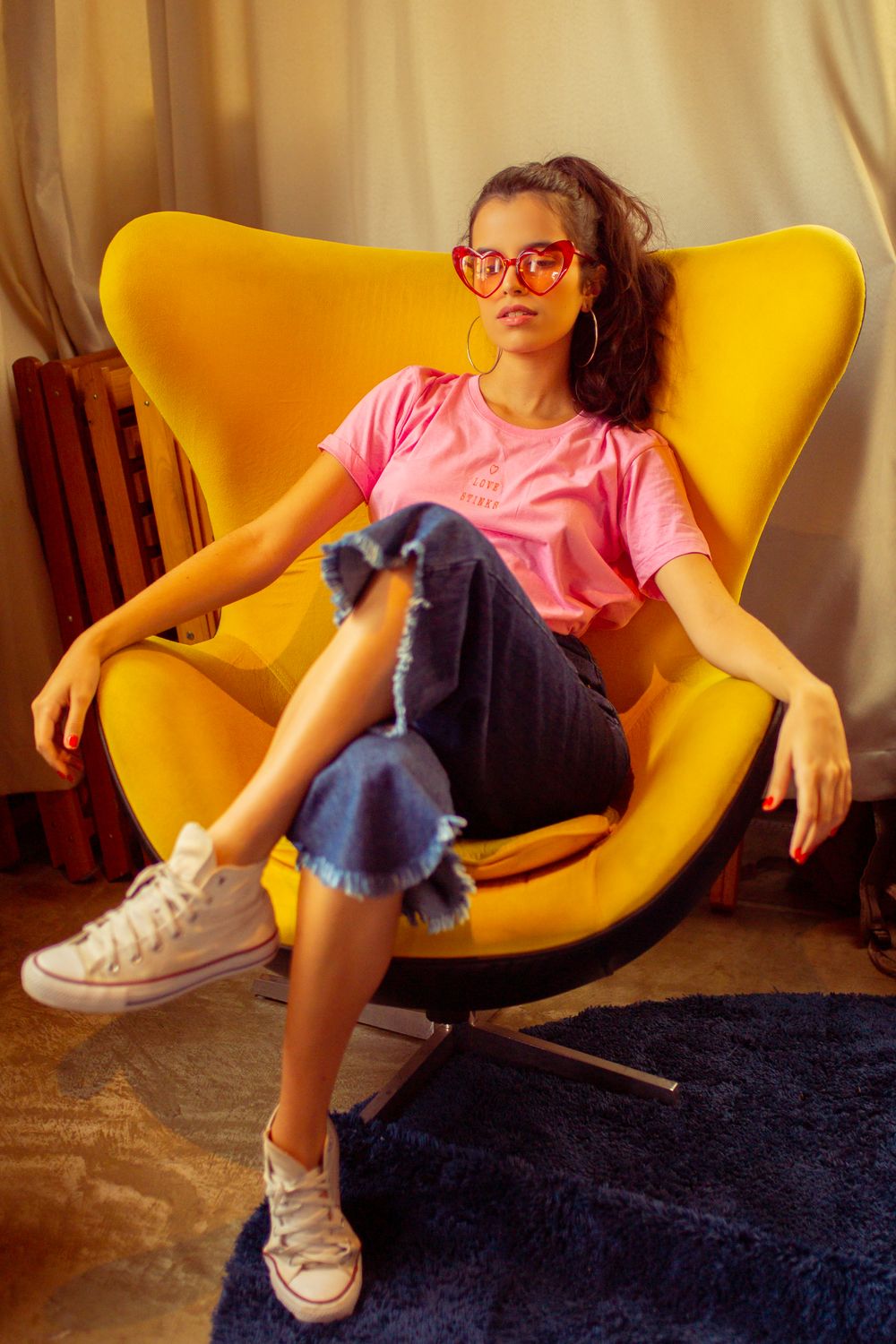 A fashionable woman in denim and pink seated confidently in a modern yellow chair.