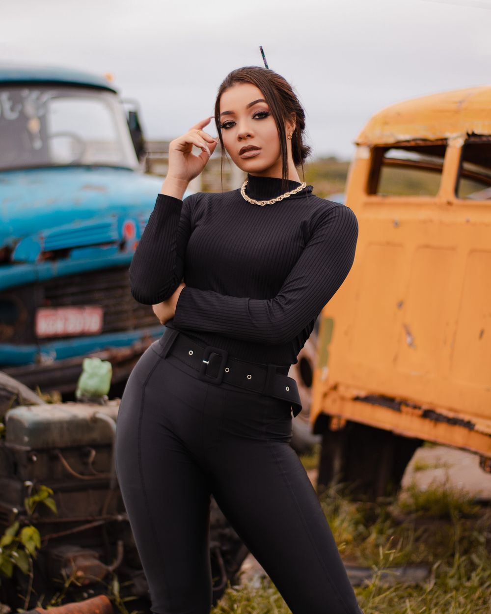 A fashionable woman poses confidently in a colorful scrapyard setting, showcasing bold style.