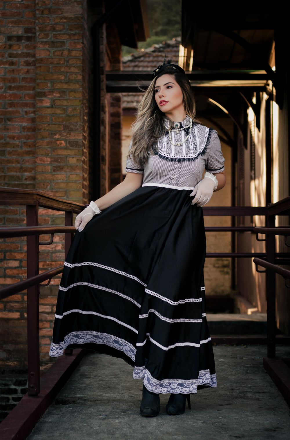 Stylish woman wearing a vintage black and white dress posing on a walkway with brick walls.