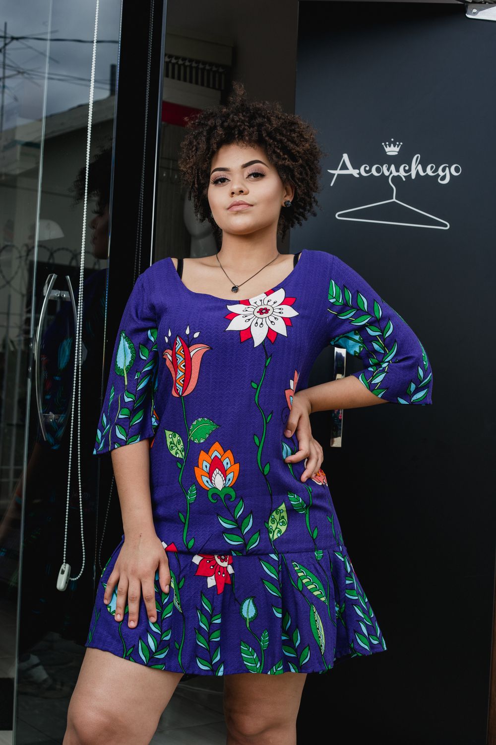 Confident woman posing outdoors in a vibrant floral dress and stylish afro hairstyle.