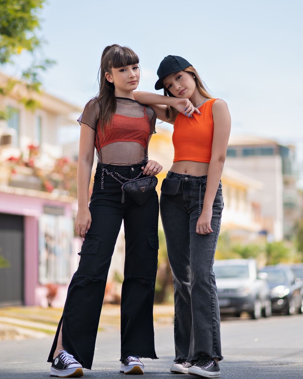 Two fashionable teenage girls pose confidently on an urban street, embracing modern youth style.