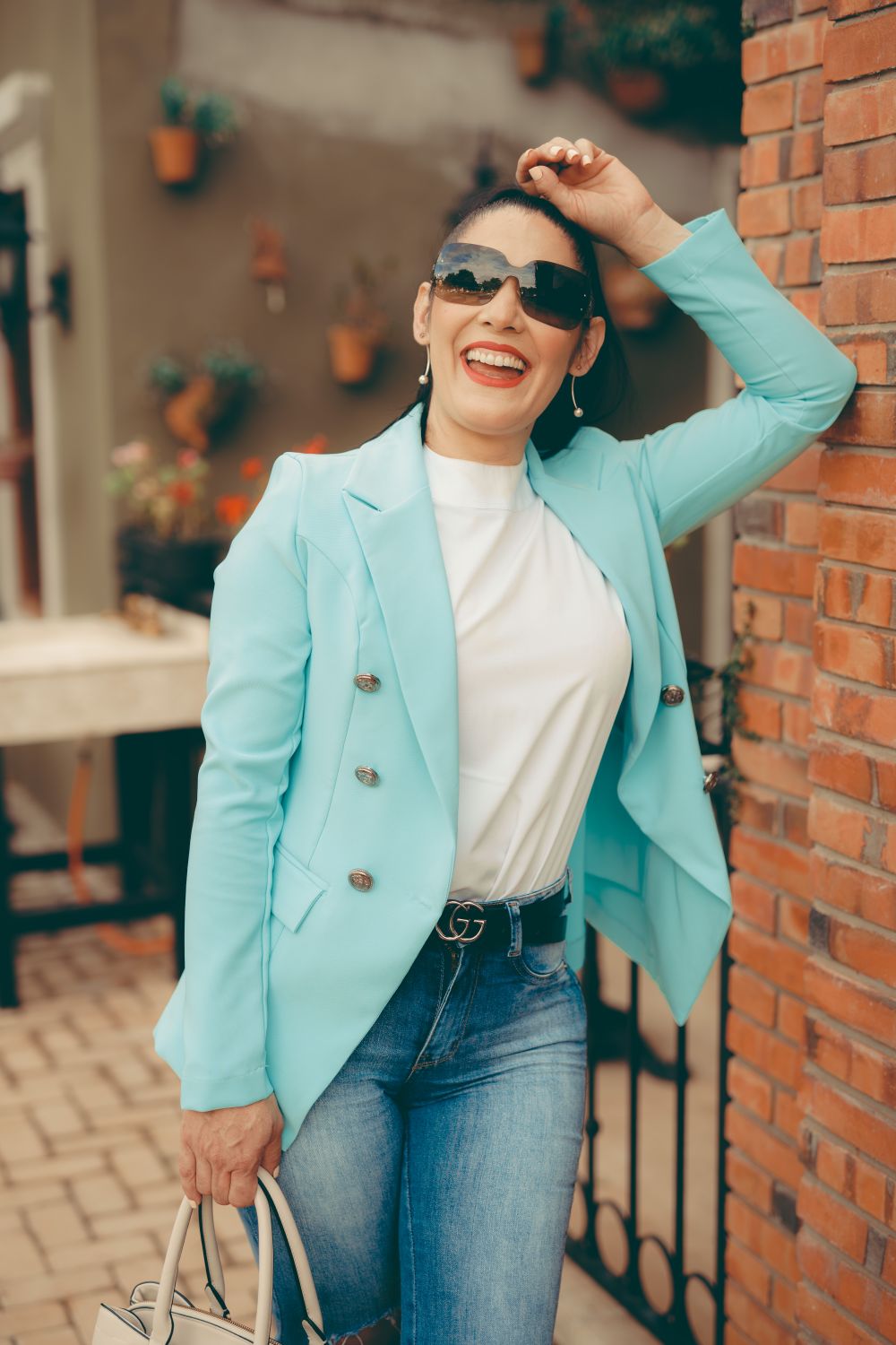 Fashionable woman in blue blazer laughing and holding a shopping bag outdoors.