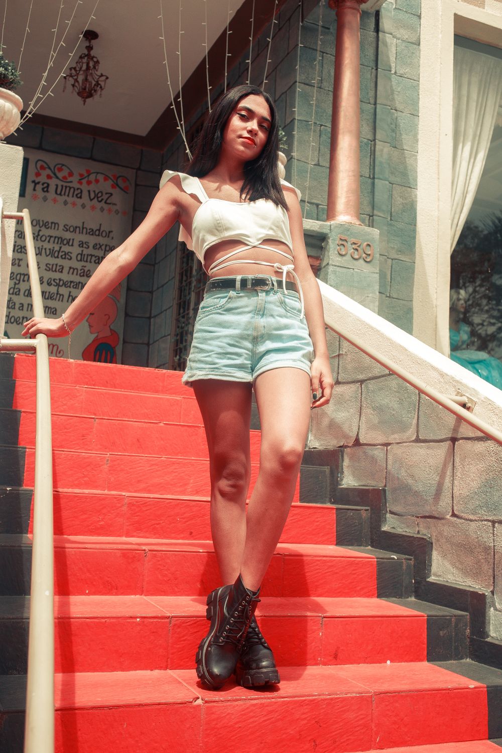 A young woman in casual summer attire posing confidently on vibrant red stairs outdoors.