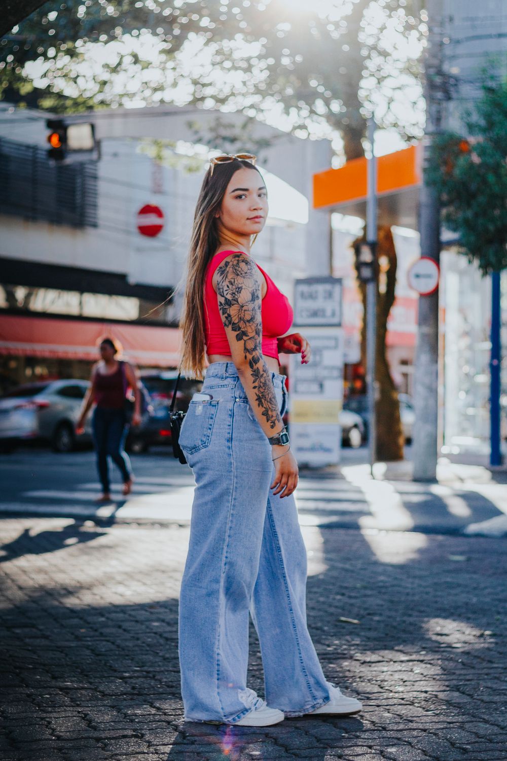 Confident woman with tattoos and casual outfit in vibrant urban environment.