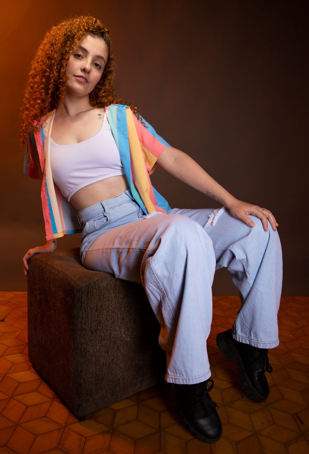 Chic studio portrait of a young woman with curly hair in a colorful crop top and jeans, exuding fashion-forward style.