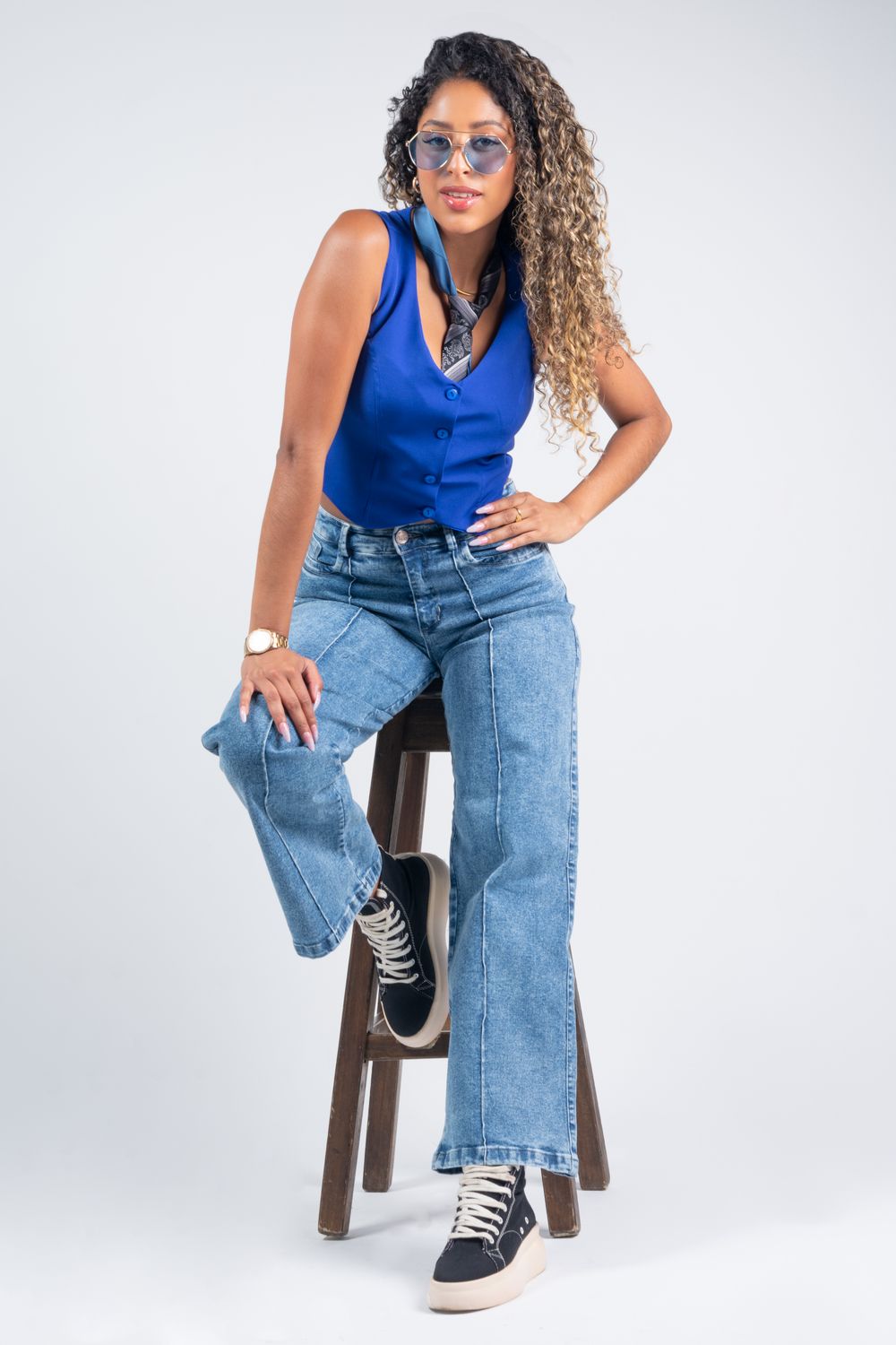 Fashionable woman posing in a studio wearing blue vest and jeans.