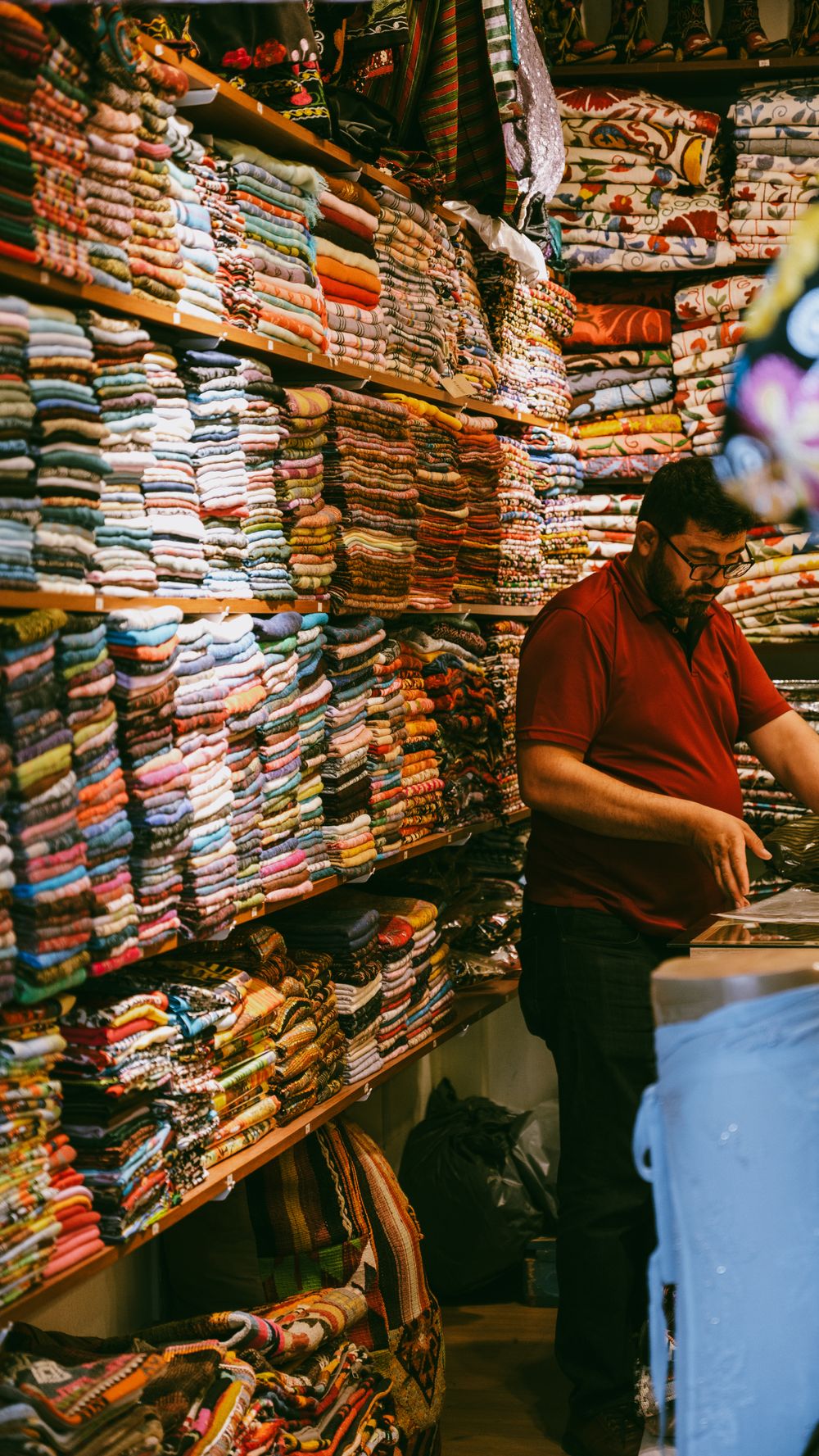 Man arranging colorful fabrics in a bustling textile store, showcasing a variety of patterns and textures.