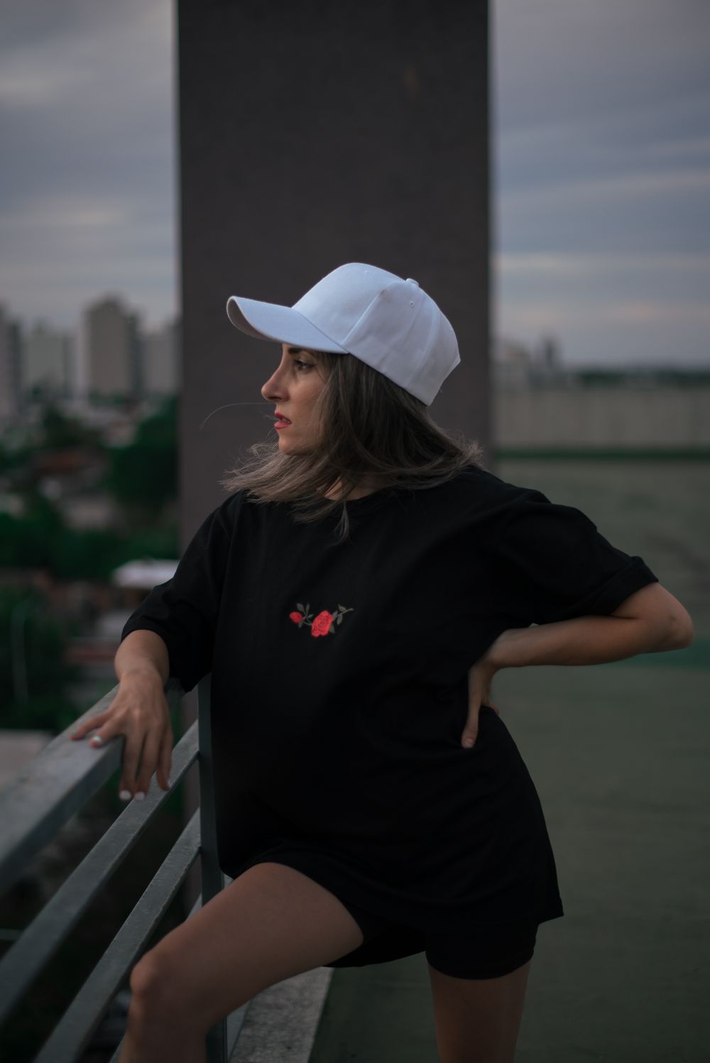 Stylish woman in urban setting wearing white cap and black outfit at twilight.