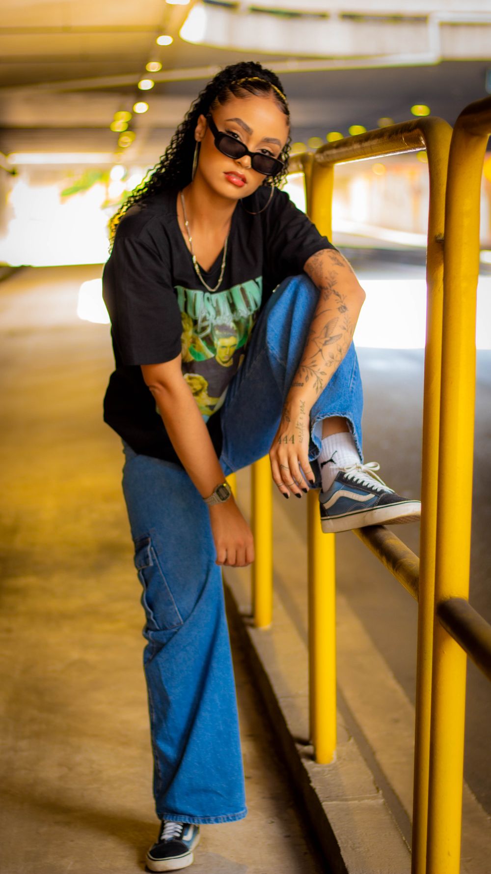 Stylish woman poses confidently in urban setting with sunglasses and denim.