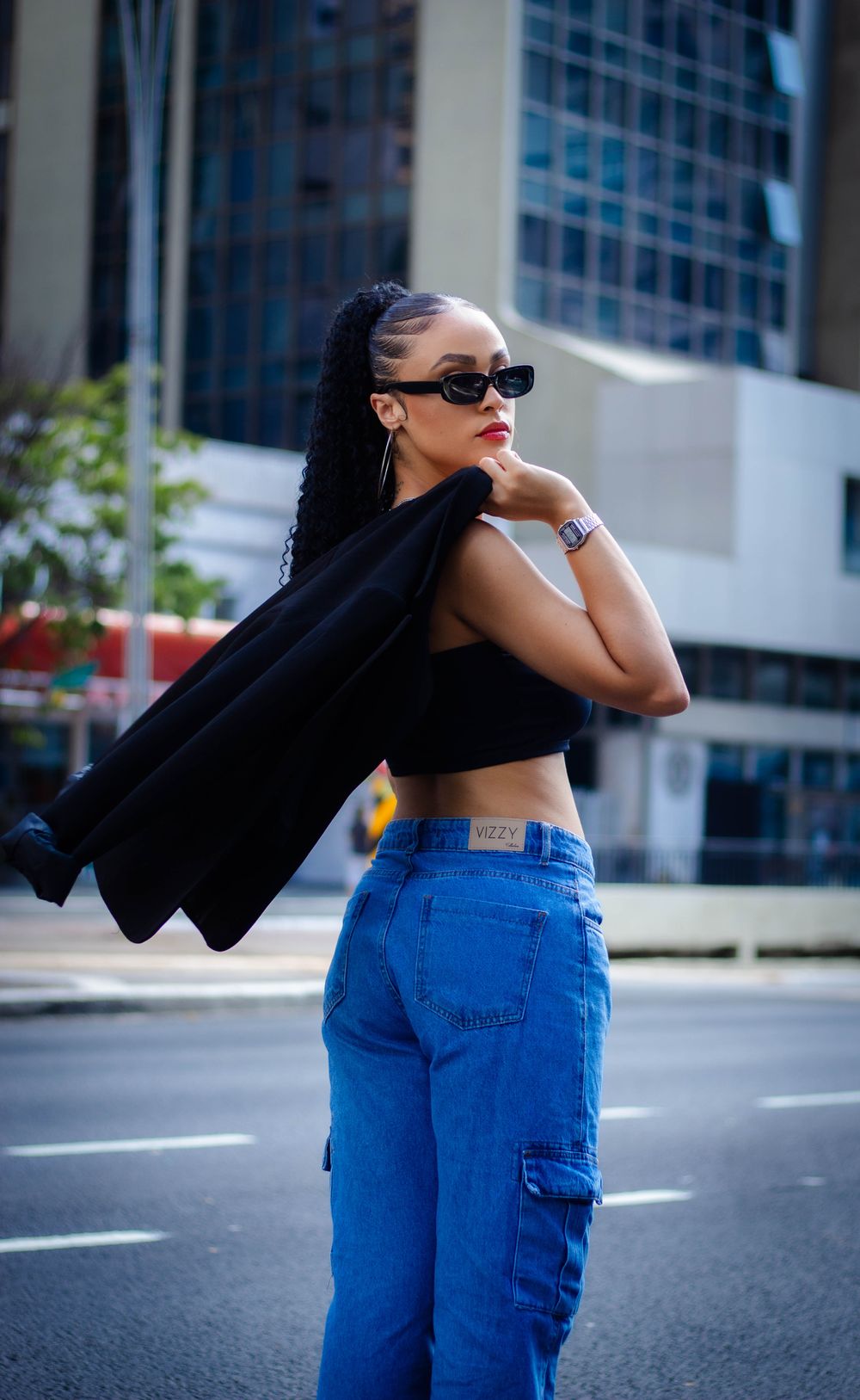 Stylish woman posing with sunglasses and jeans by city buildings.