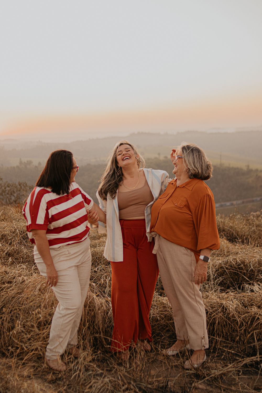 Three women sharing a joyful moment on a meadow, São Paulo, Brazil, during sunset.