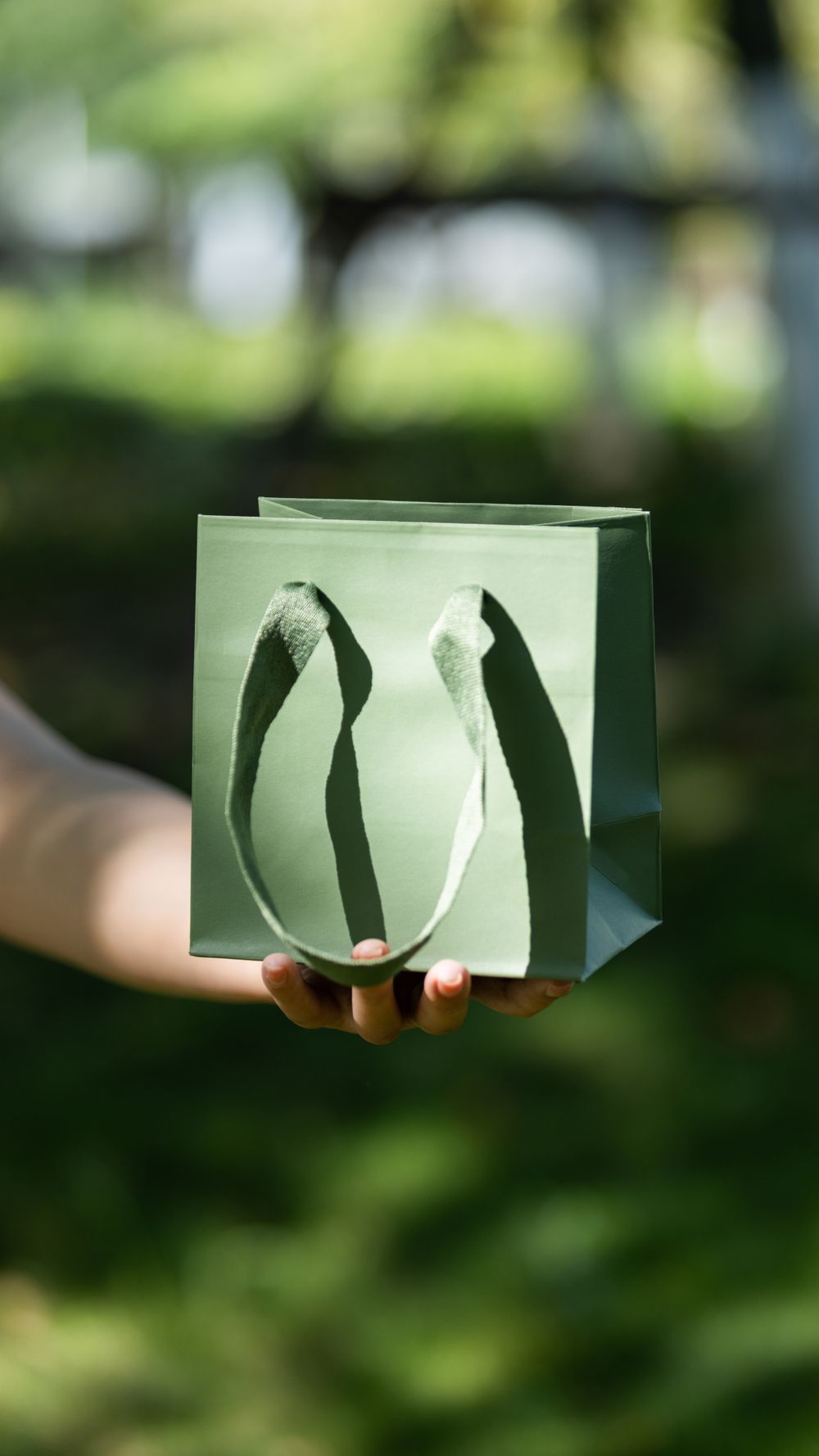 A hand holding a small green gift bag outside in natural sunlight, showcasing simplicity and elegance.