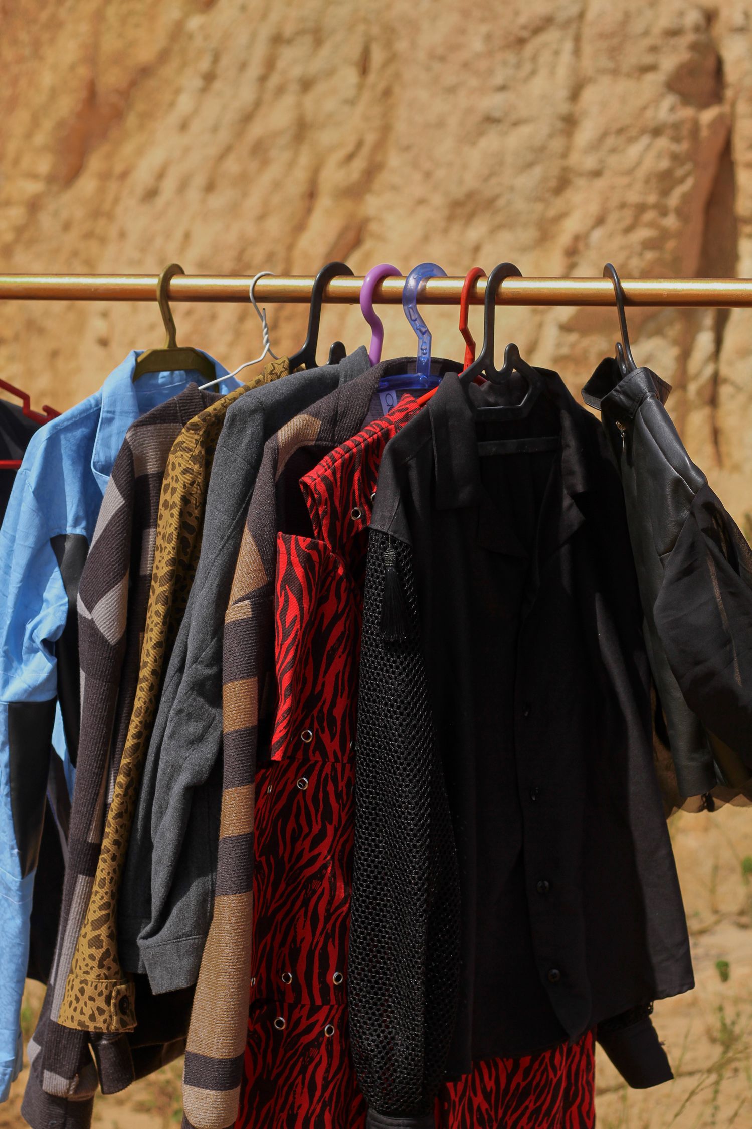Vibrant clothing array on hangers outdoors against arid backdrop.