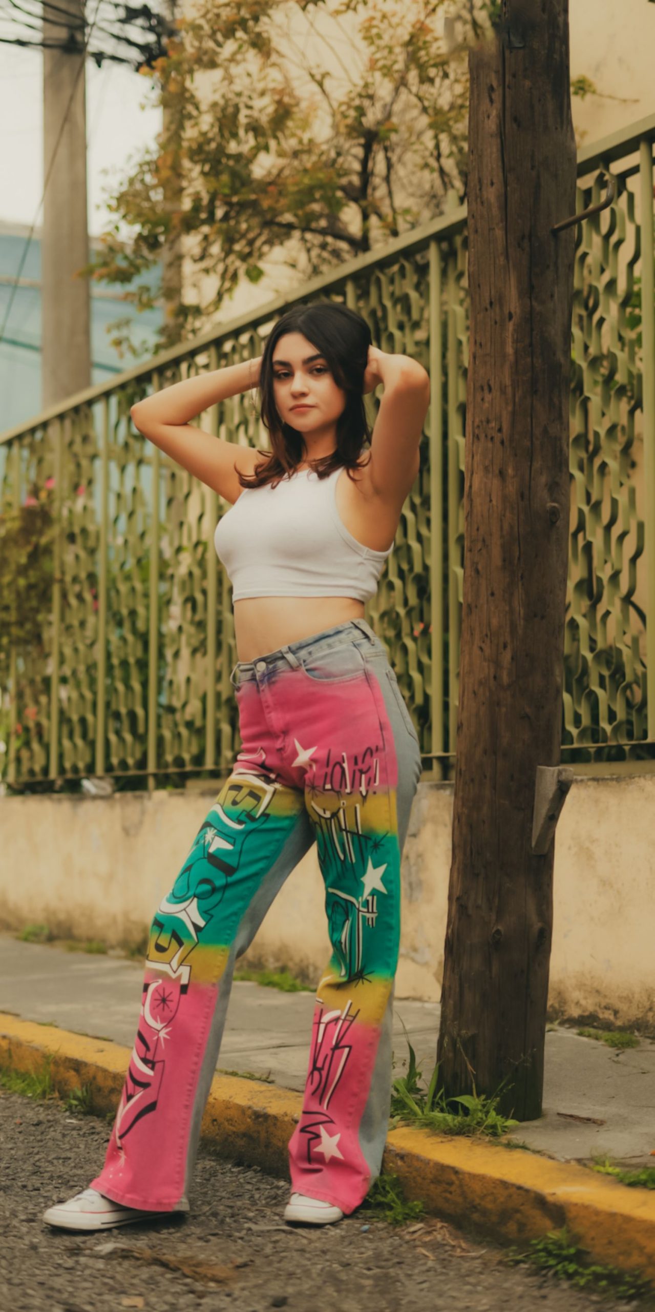 Stylish young woman poses confidently on an urban street in vibrant fashion, showcasing colorful jeans and a trendy look.