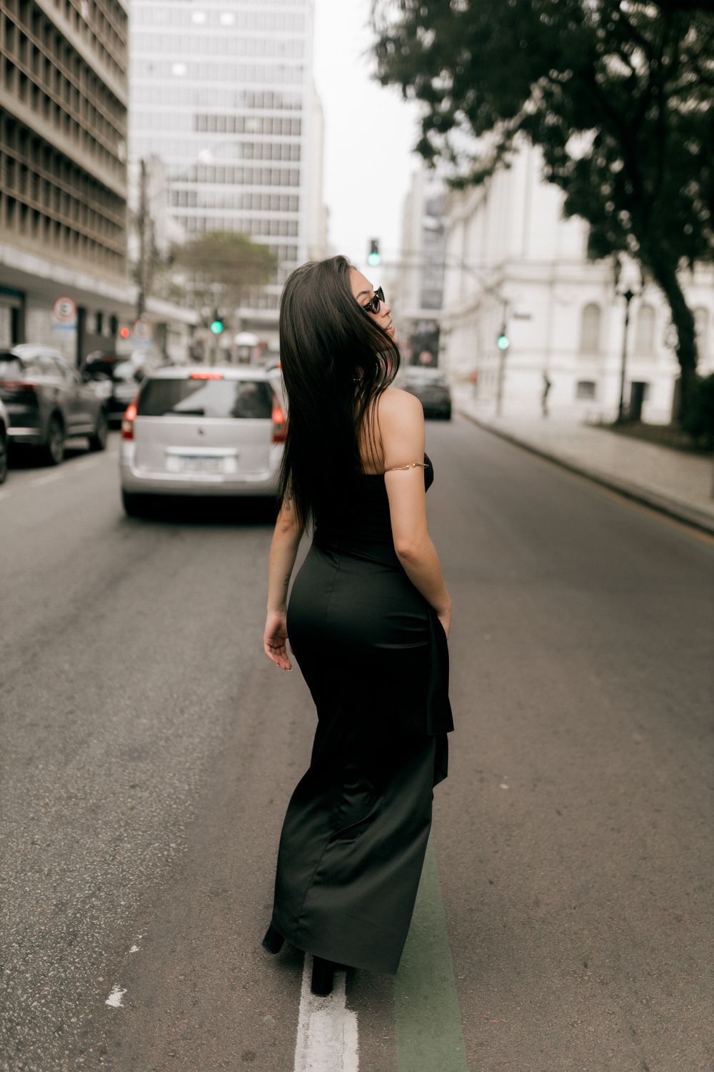 Stylish woman in black dress walking down busy city street, creating a chic urban vibe.