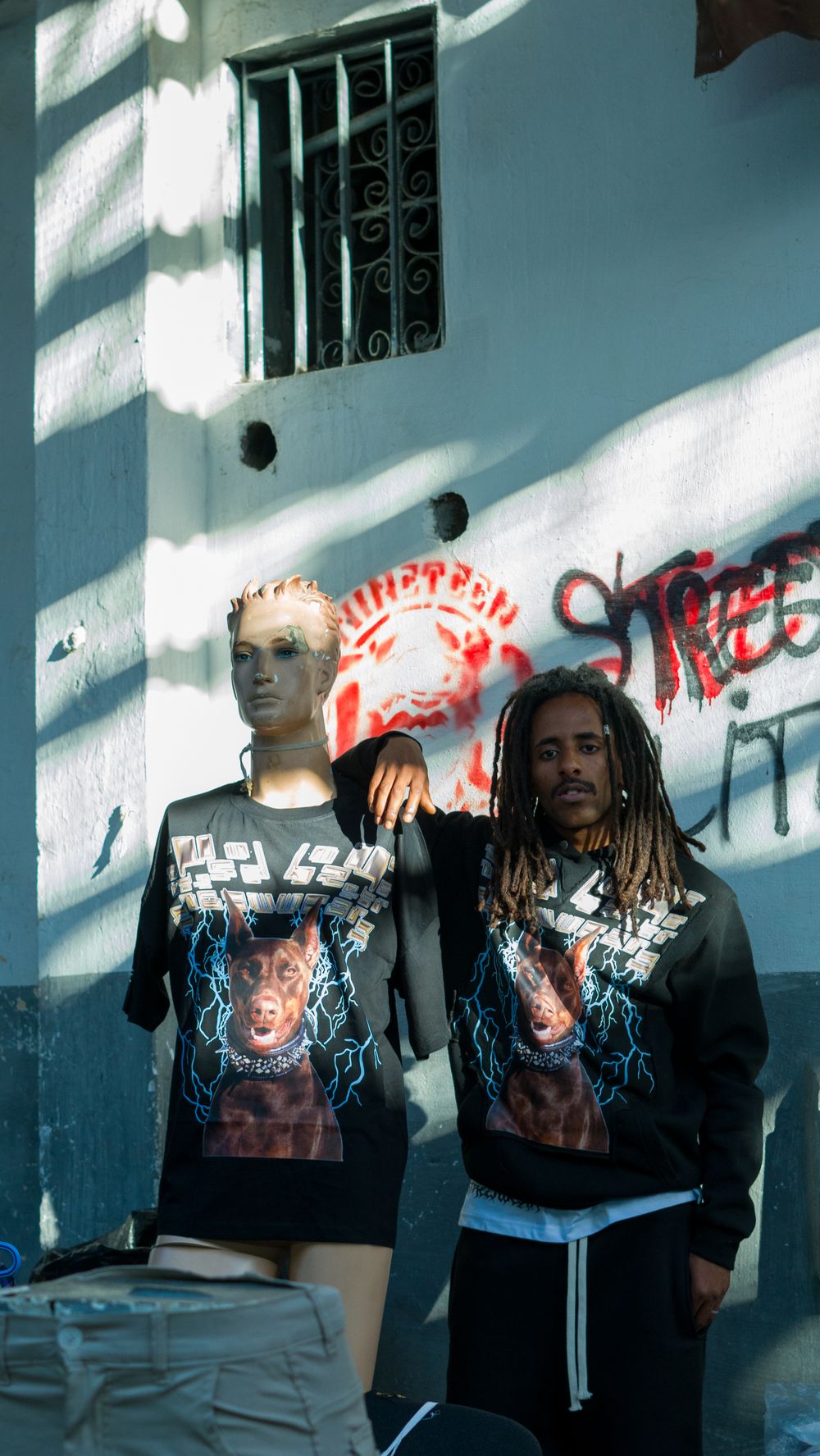 Man and mannequin in matching streetwear pose against graffiti wall in Morocco.