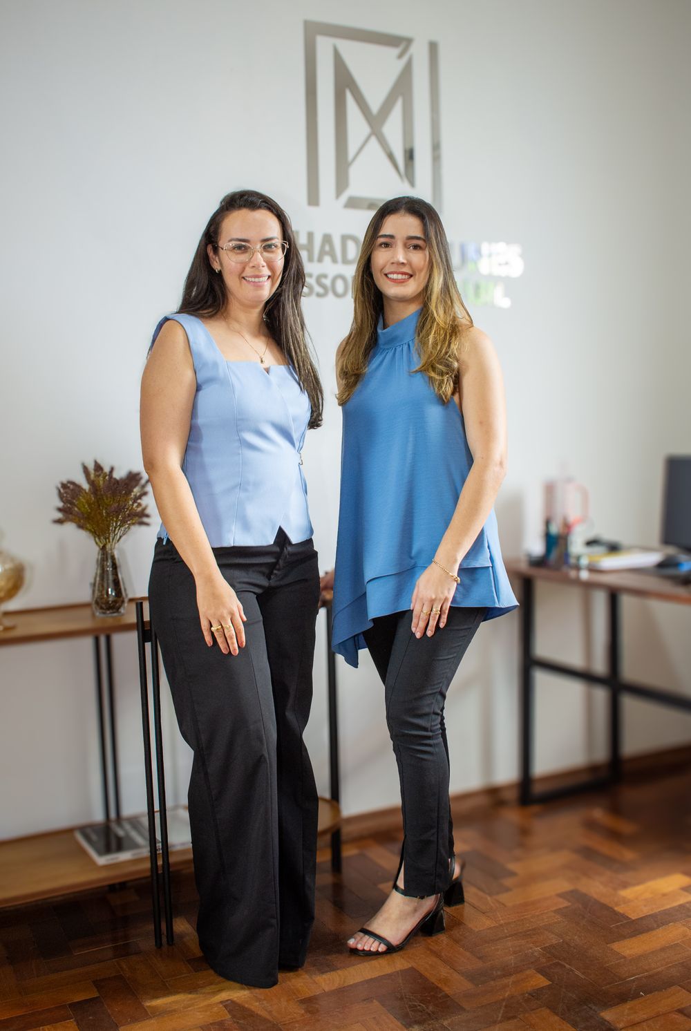 Two professional women pose confidently in a modern office in Tiros, Brazil.