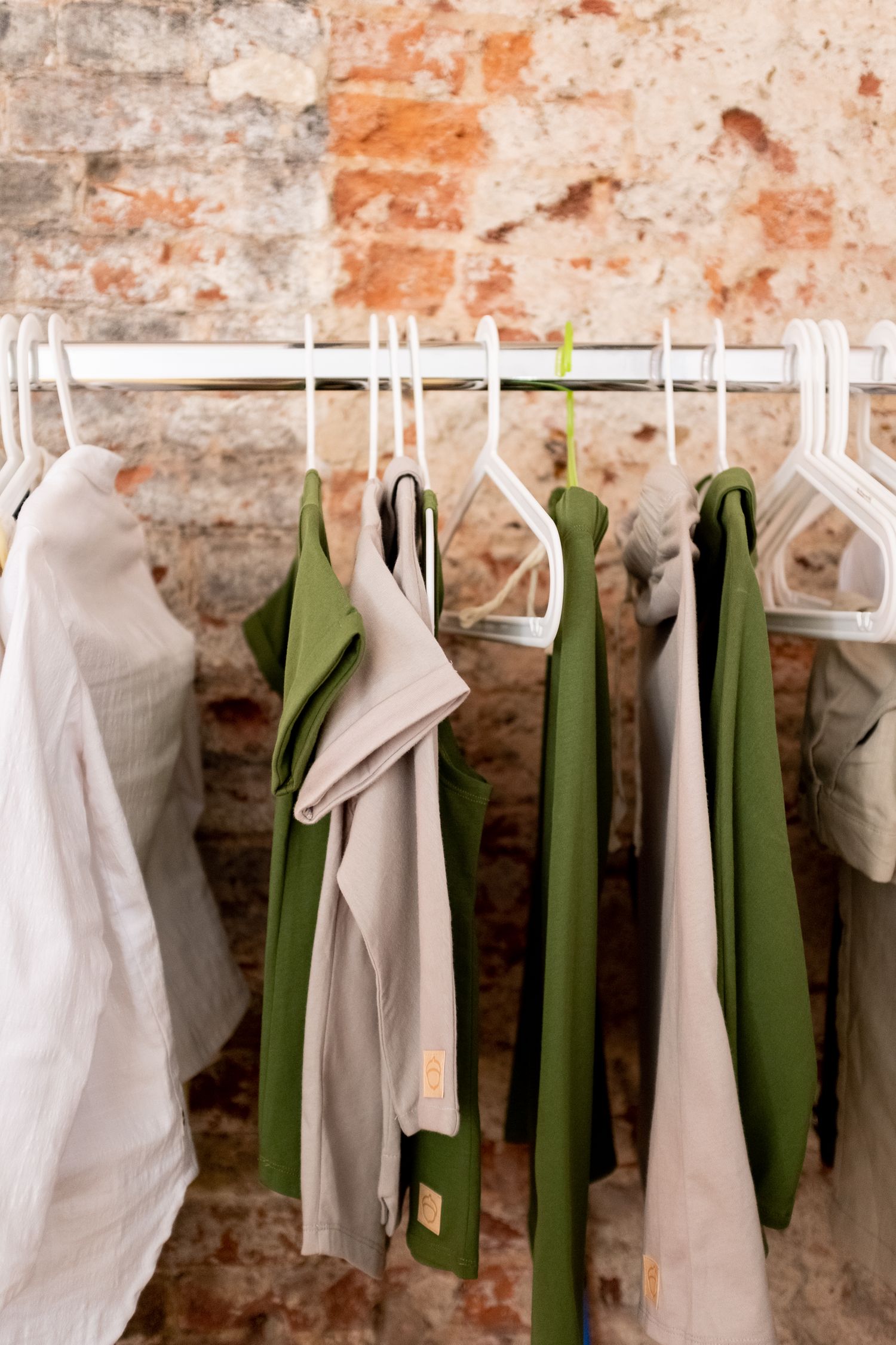 Green and white clothing on hangers against a rustic brick wall indoors.