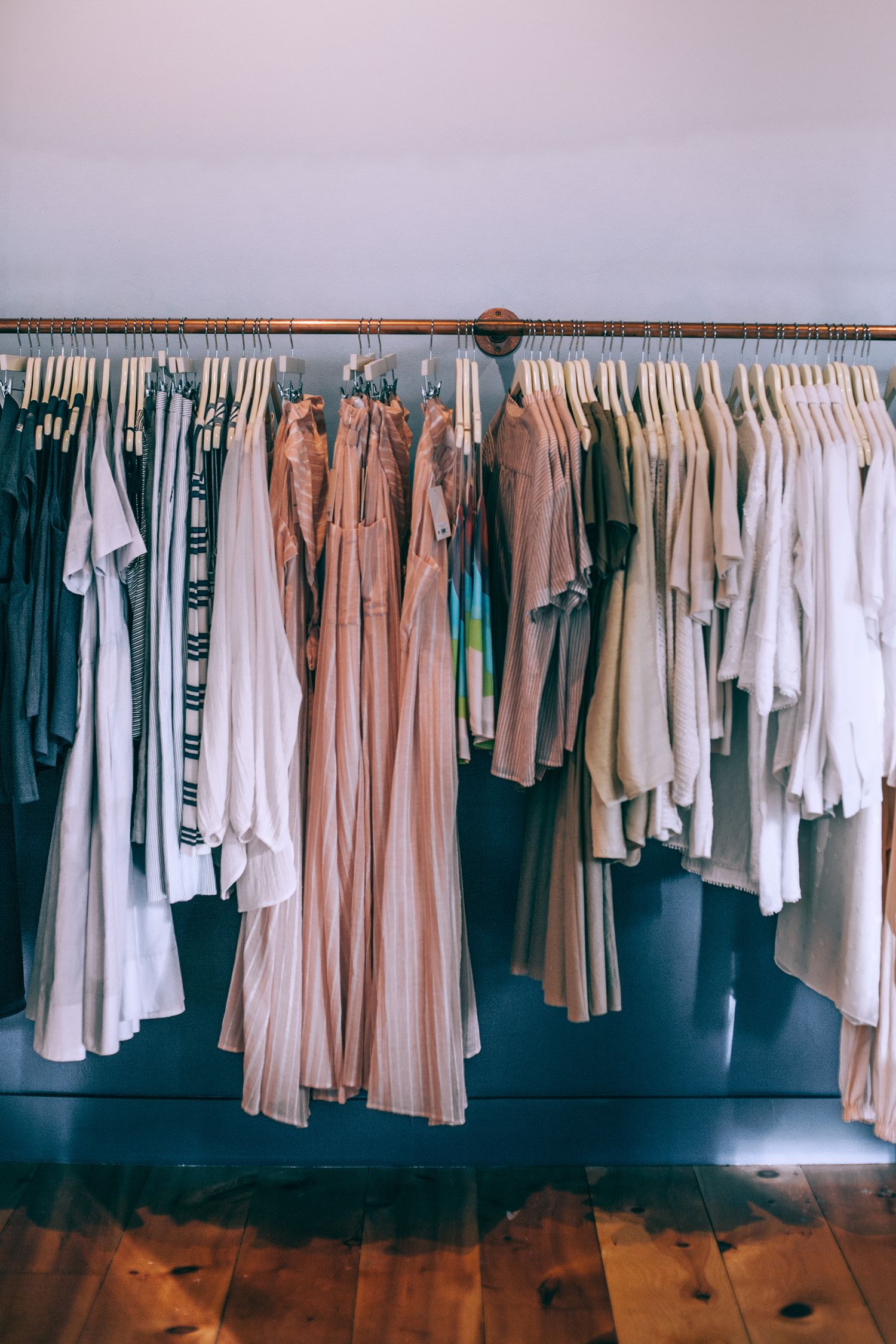 Various dresses and t shirts on hangers near wall in clothing store with wooden floor