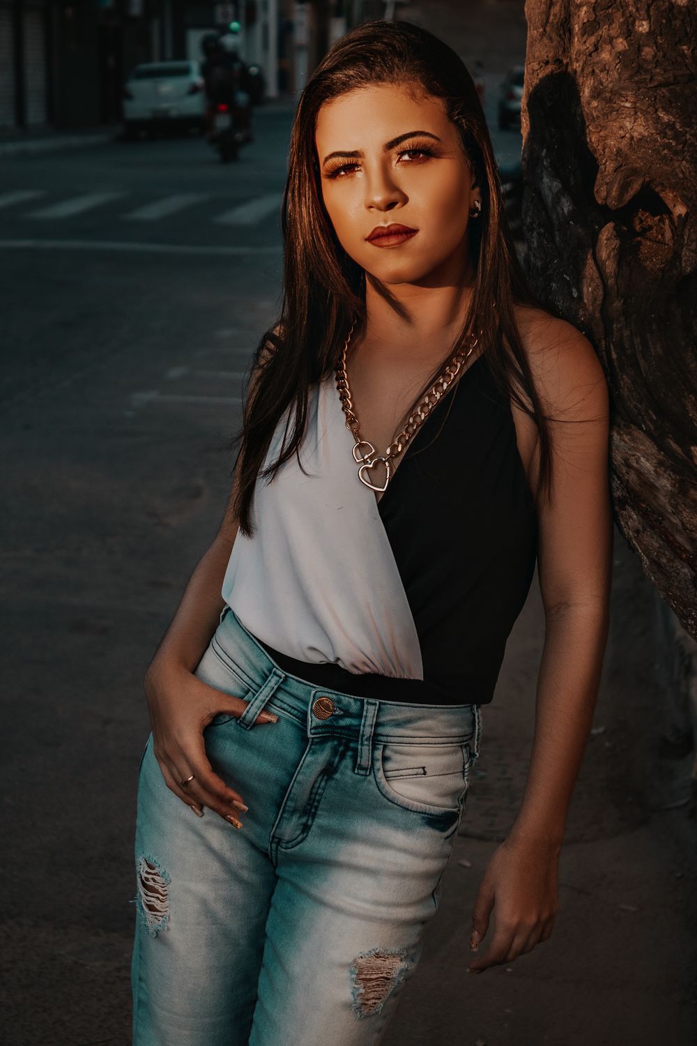 Confident woman in ripped jeans and a tank top posing outdoors in urban street lighting.