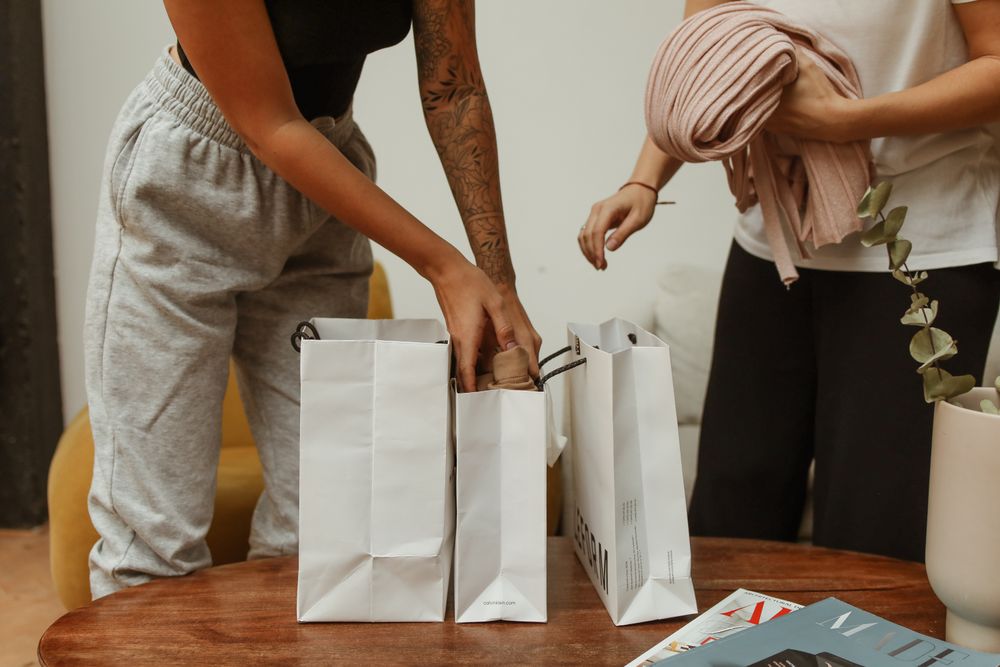 Two young adults unpacking shopping bags with clothing in a cozy indoor setting.