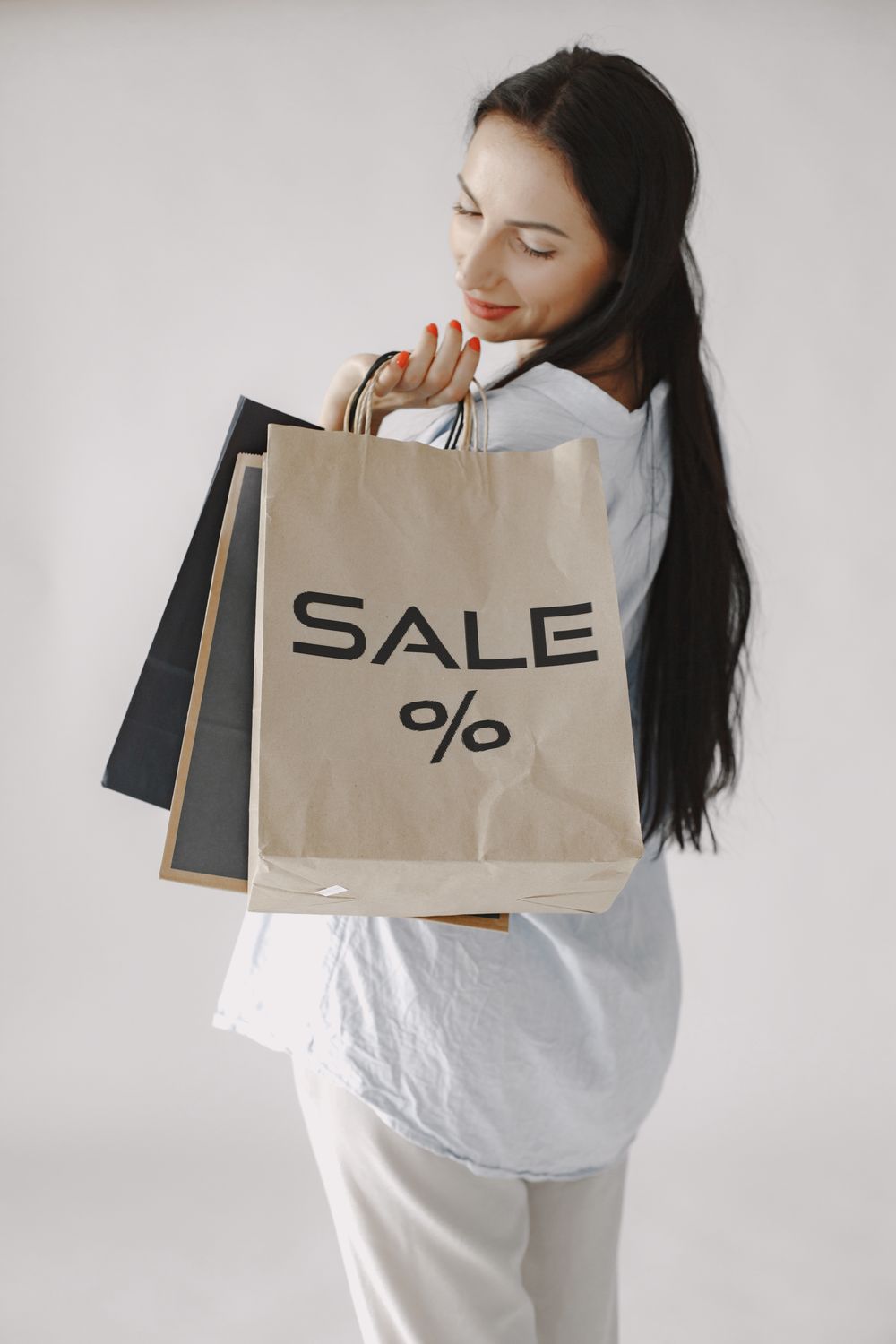 Smiling woman holding shopping bags marked 'SALE' against a white background.