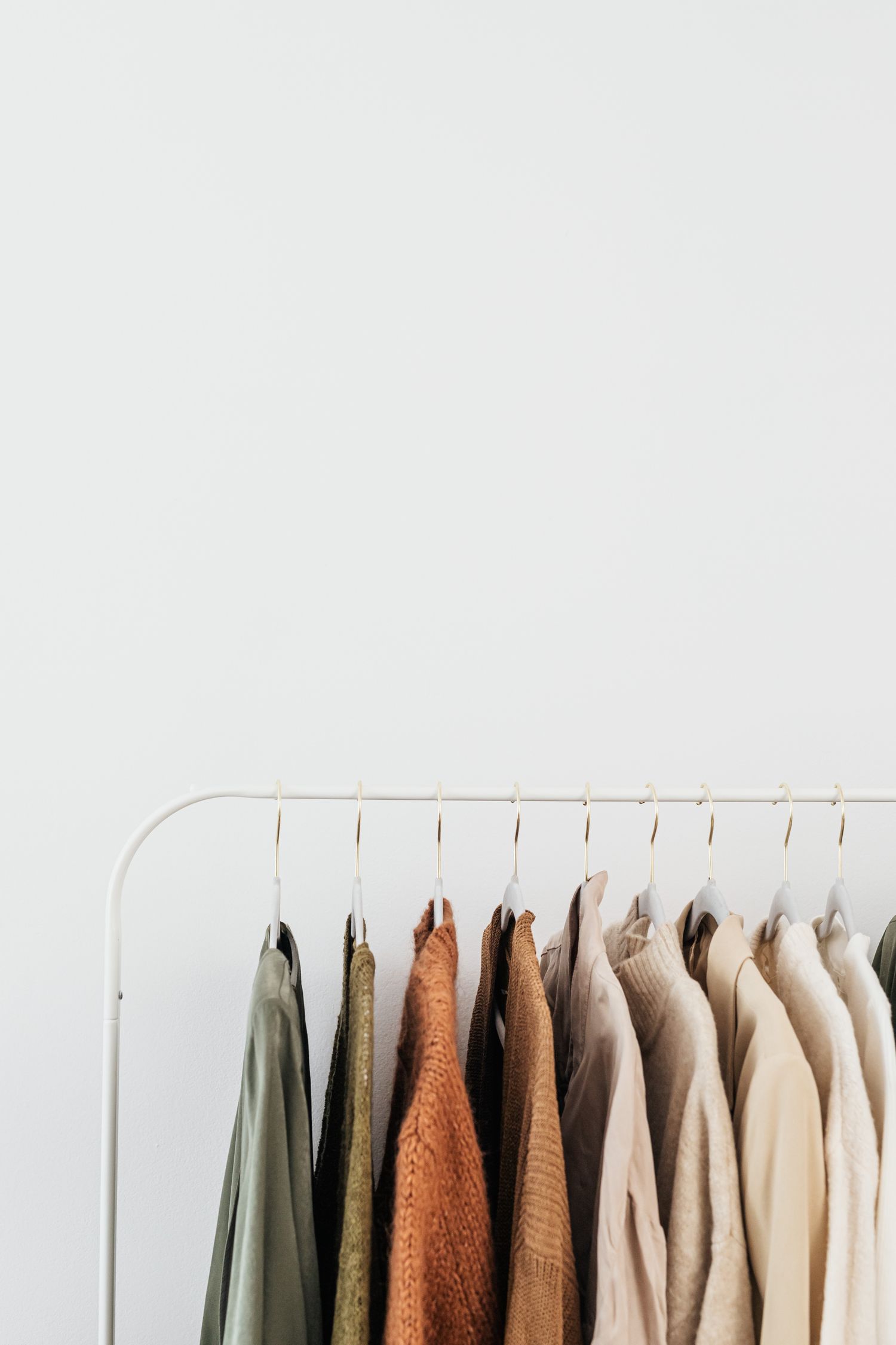 Elegant neutral-toned clothes hanging on a white rail against a plain background, perfect for fashion themes.