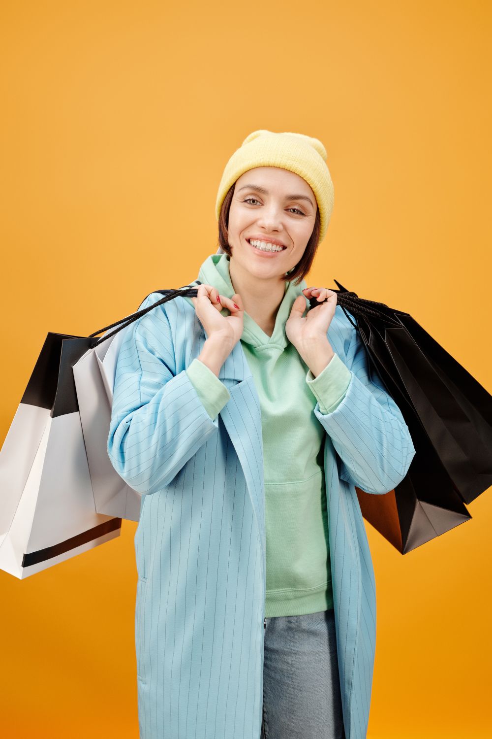 Cheerful young woman in vibrant colors holding multiple shopping bags against an orange backdrop.