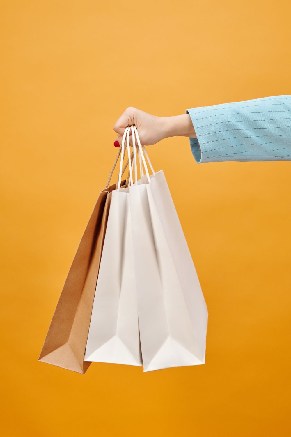 Close-up of a hand holding shopping bags against a bright yellow background, perfect for retail concepts.