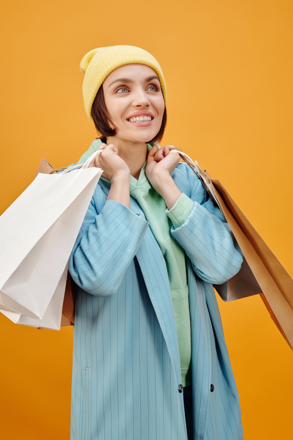 Happy woman dressed in vibrant clothing holding shopping bags with a yellow backdrop.