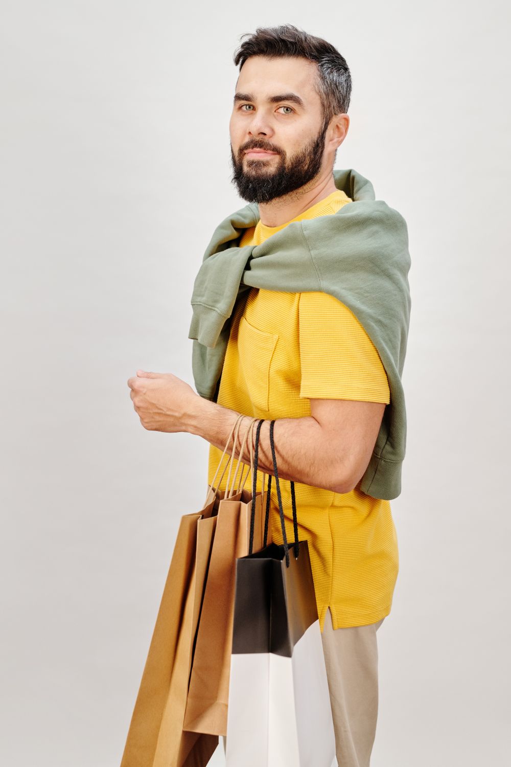 Adult man in casual attire holds shopping bags against a neutral background, showcasing a modern fashion vibe.