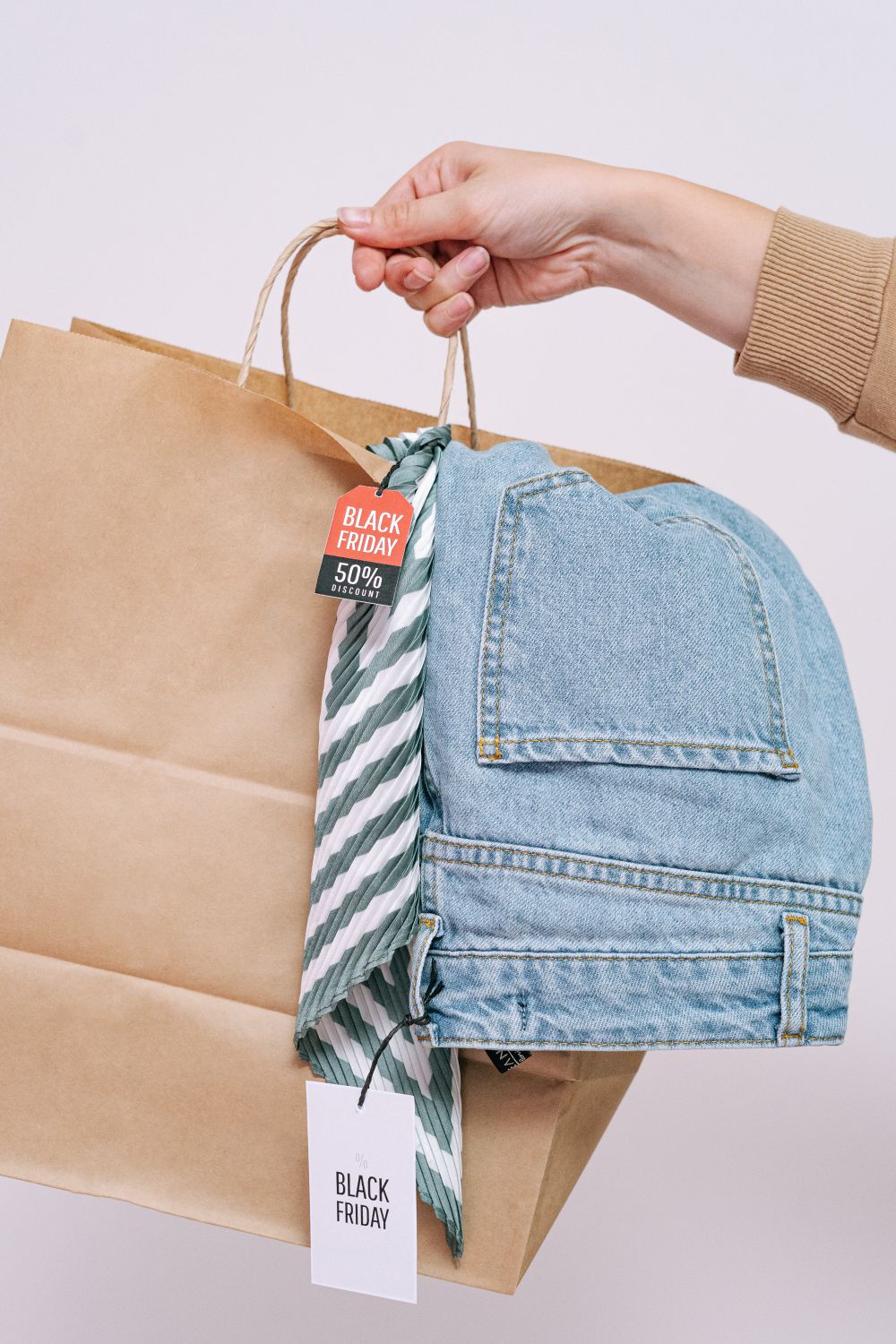 Close-up of a hand holding a shopping bag with denim jeans, perfect for Black Friday sales.