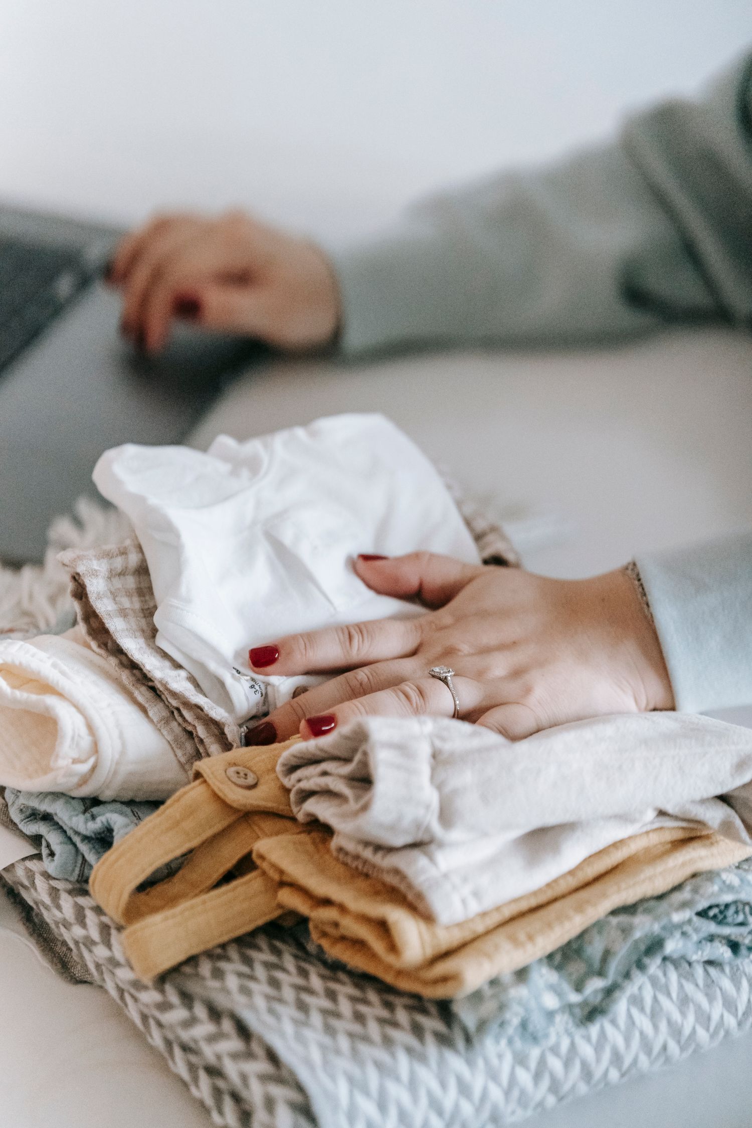 Woman's hands folding a cozy stack of different textiles indoors. Warm tones.