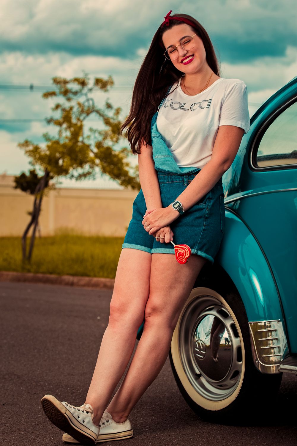 Woman smiling and leaning on a blue vintage car outdoors in Birigui, Brazil.