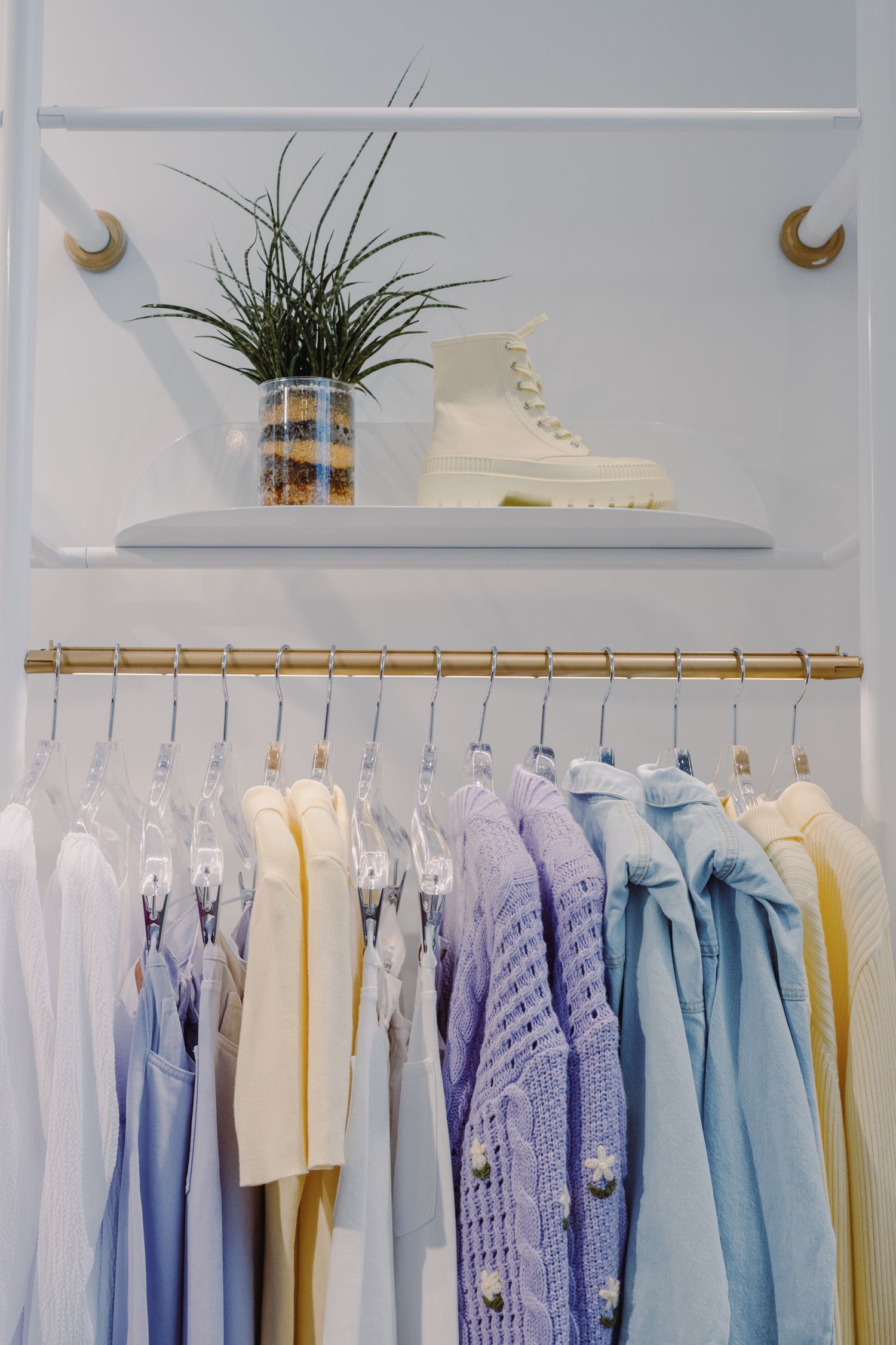 A stylish display of pastel clothes on hangers in a modern boutique with fashion boots and a decorative plant.