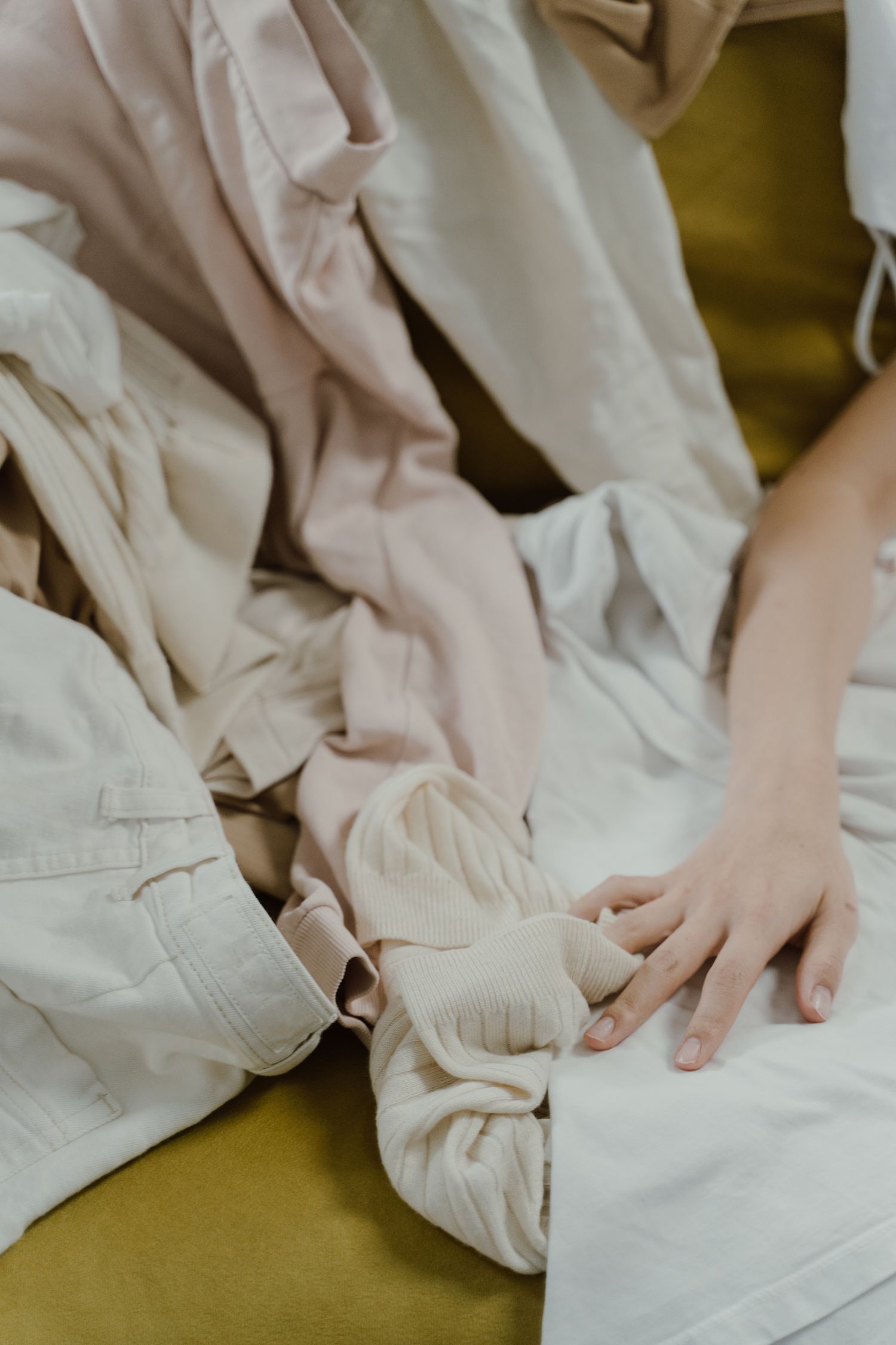 A soothing arrangement of soft, neutral-toned clothes with a hand gently resting on them.