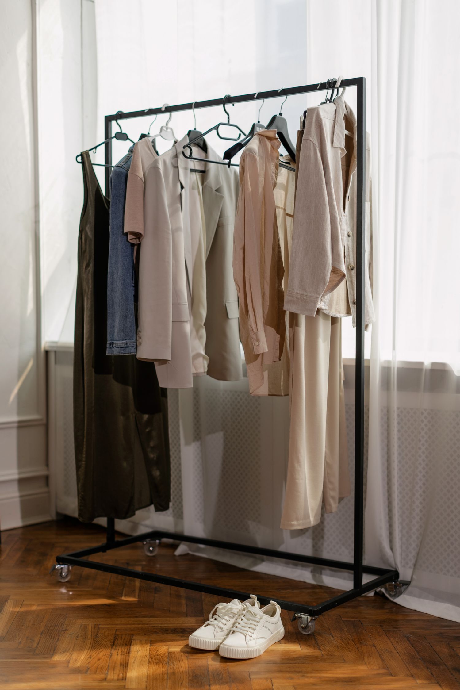 A minimalist clothing rack with neutral outfits and white sneakers in a bright room.