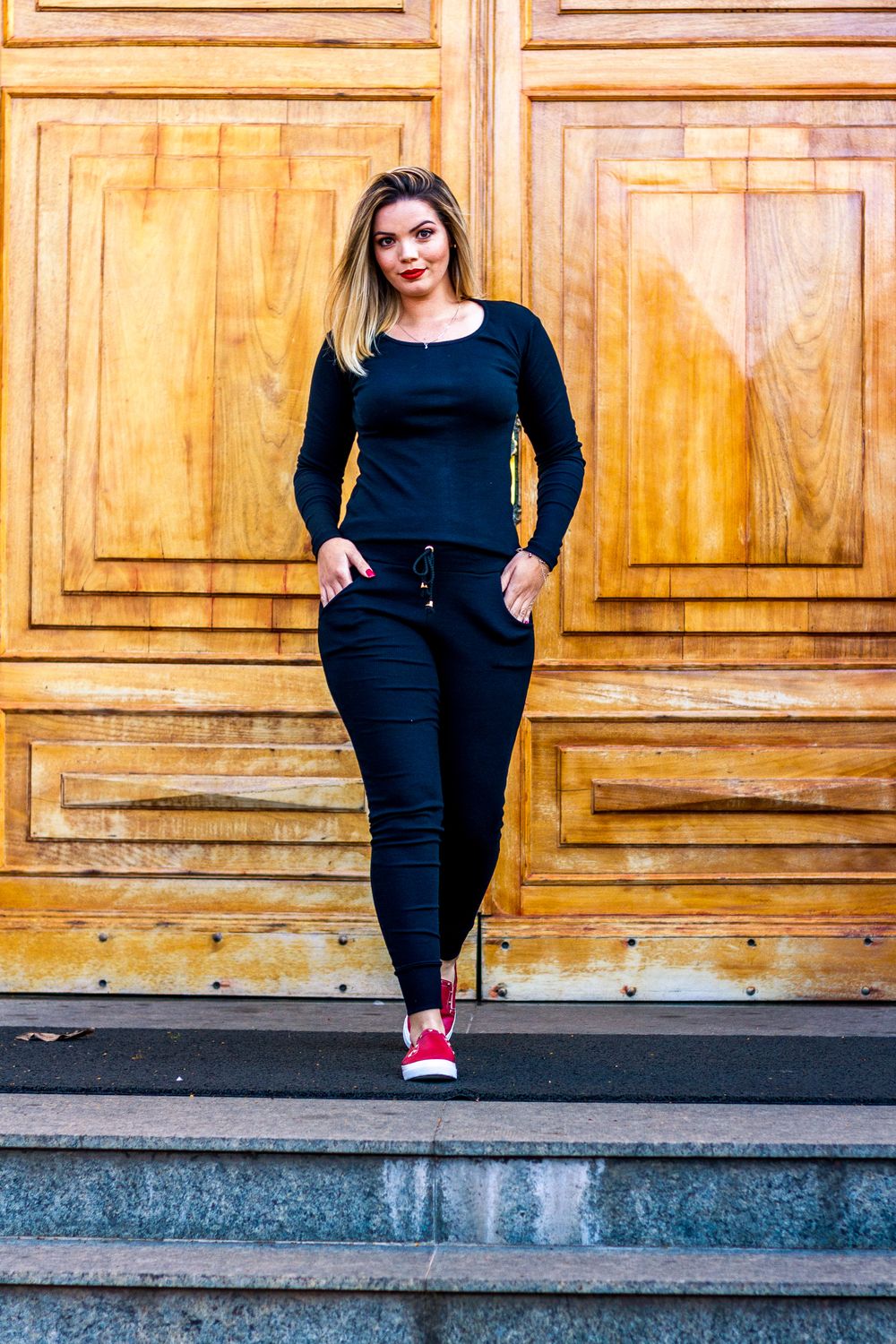 Confident woman in a black outfit posing outdoors in Sorocaba, Brazil against wooden doors.