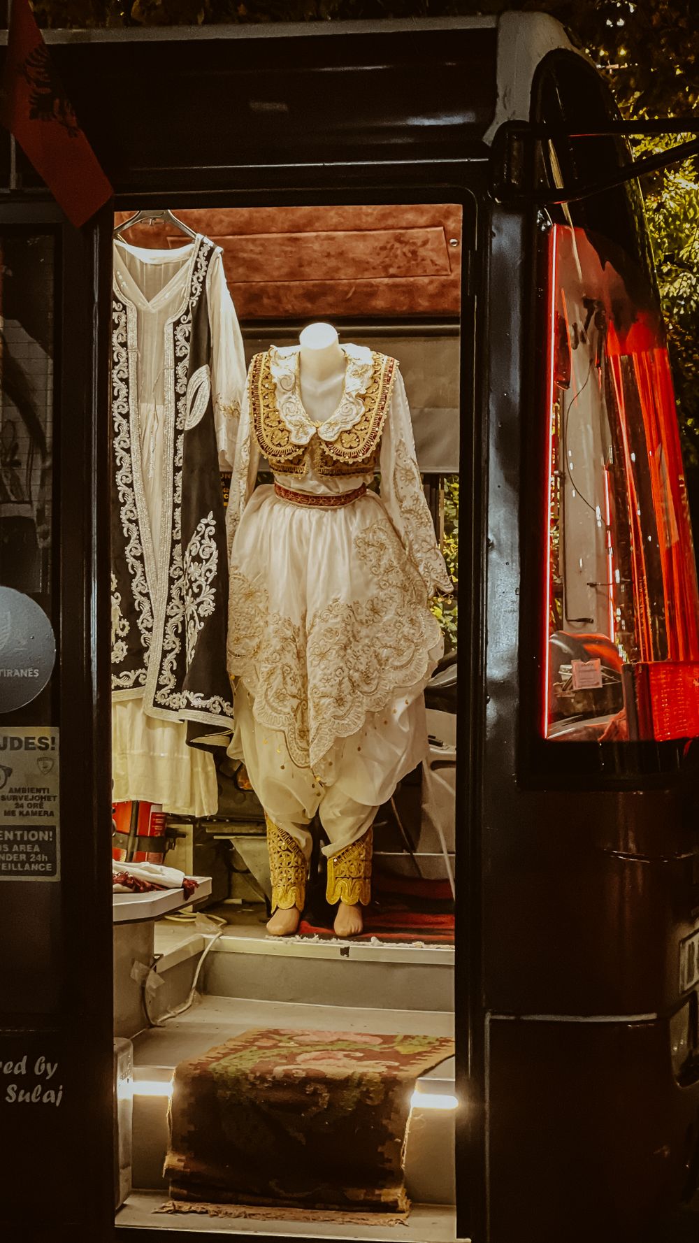 Traditional Albanian attire on a mannequin inside a vehicle entrance at night.