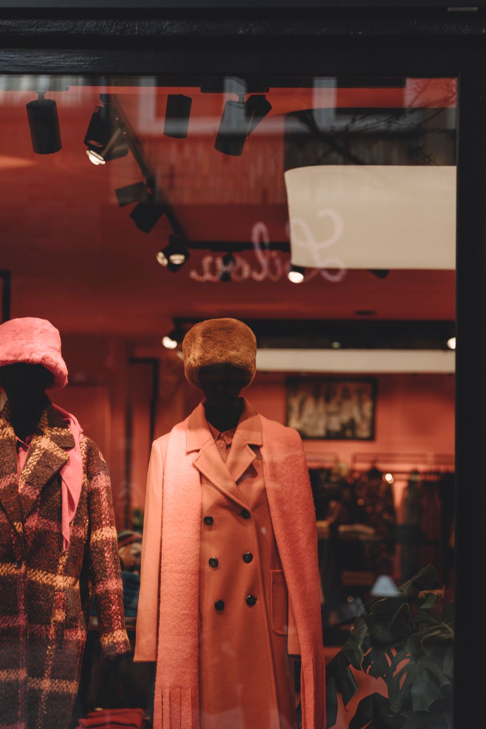 Elegant winter coats and hats displayed on mannequins in a stylish boutique window.
