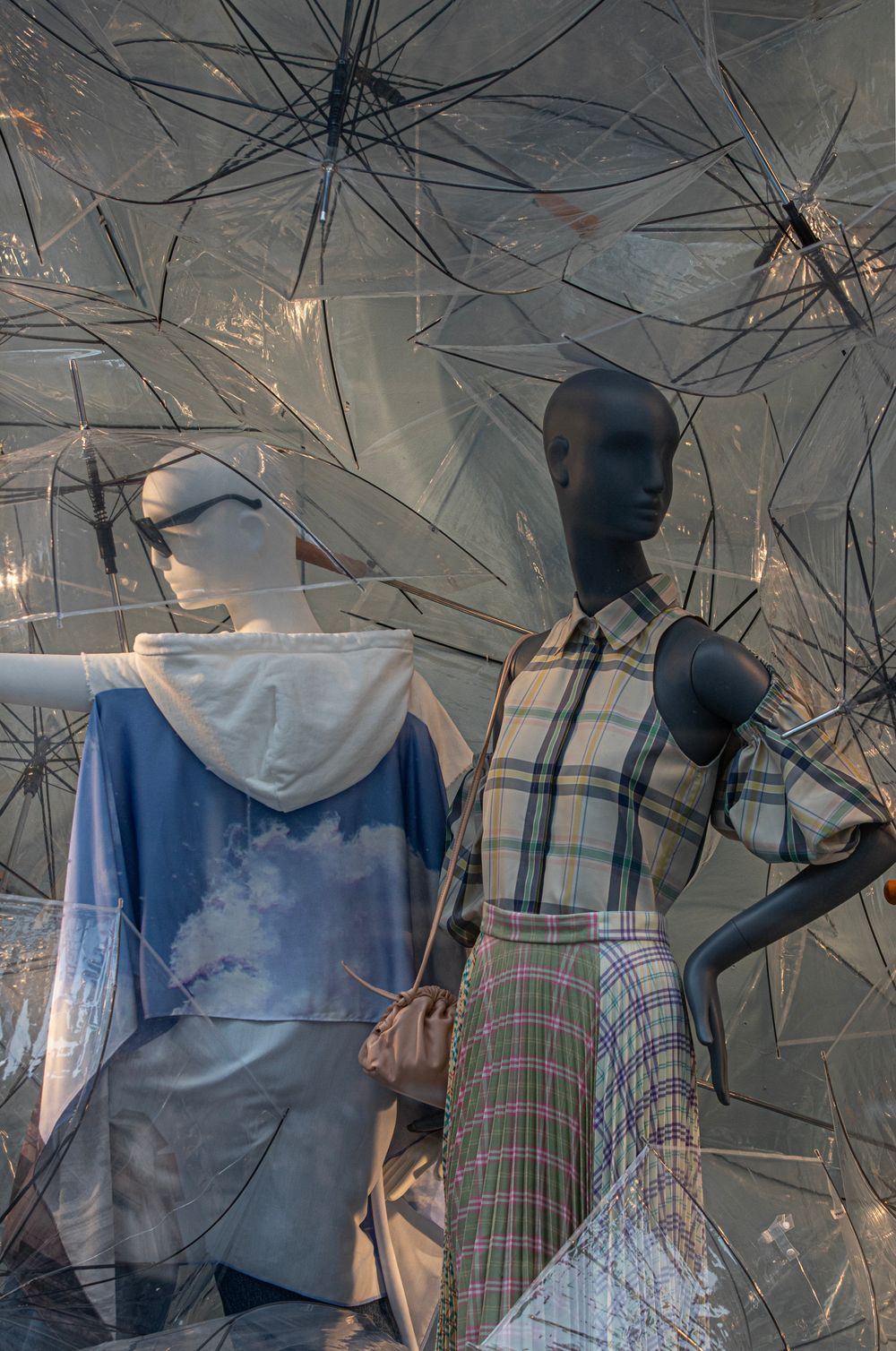 Stylish mannequins in a Manhattan store window featuring plaid fashion and transparent umbrellas.