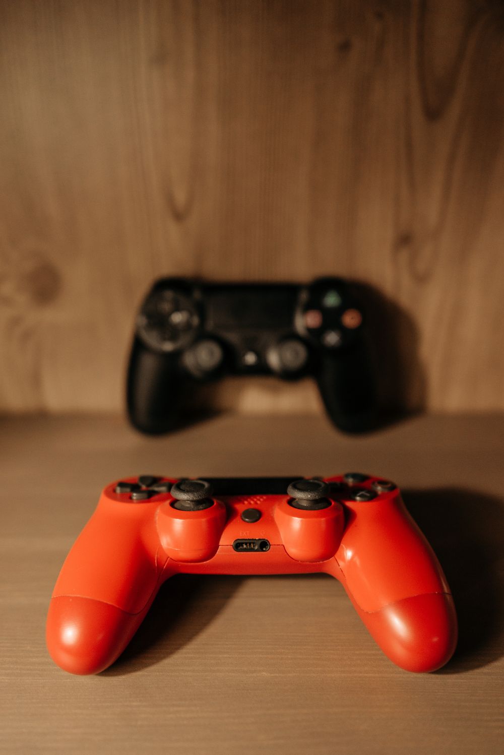 Red and black game controllers on a wooden surface with a soft focus effect.
